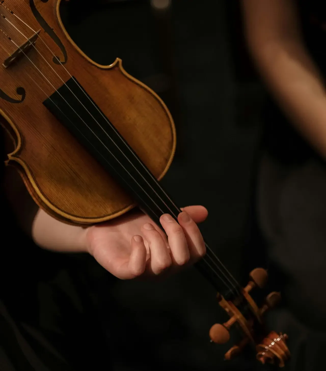 An artistic close-up of a hand holding a violin during a performance.