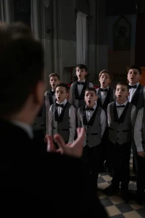 A choir of boys performing indoors under direction, wearing formal attire.