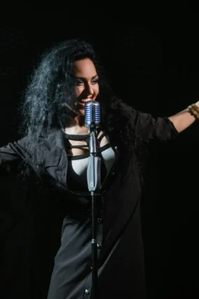 Dynamic shot of a female vocalist in a black dress singing passionately into a microphone.